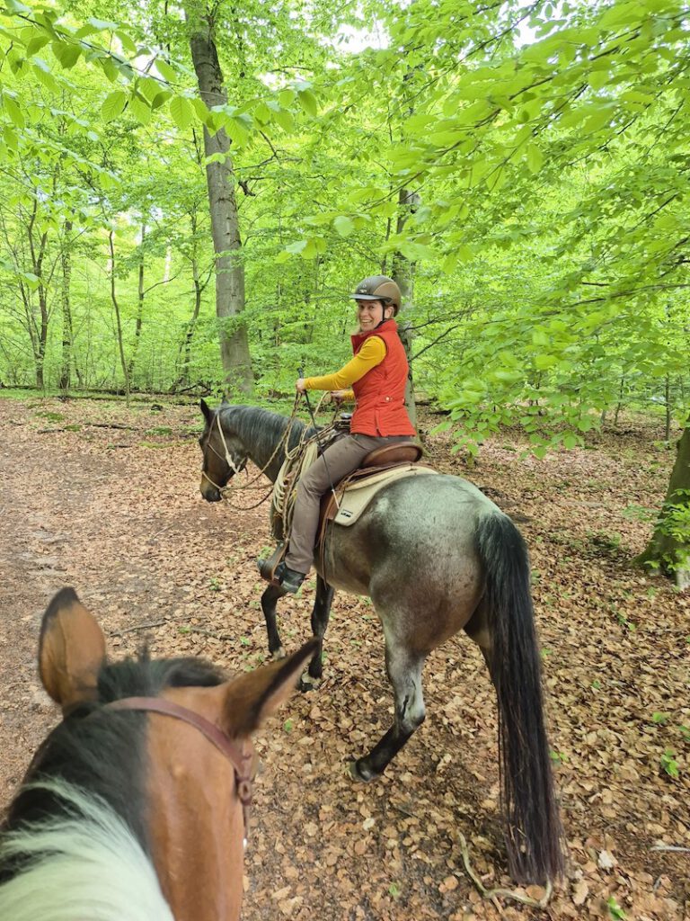 Sicher ausreiten gehen: Eine Reiterin im Wald dreht sich nach ihrer Mitreiterin um